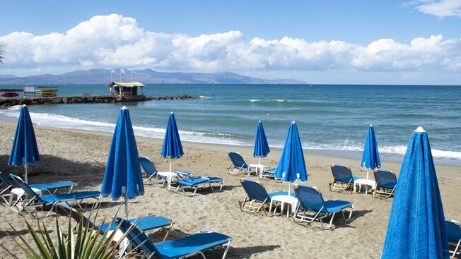 An array of recliners and umbrellas on a beach with a jetty
