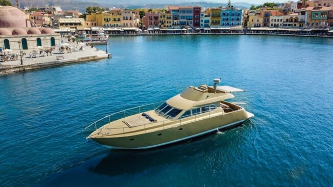 A luxury yacht in the water near a vibrant, colorful harbor lined with historic buildings in Chania, Greece