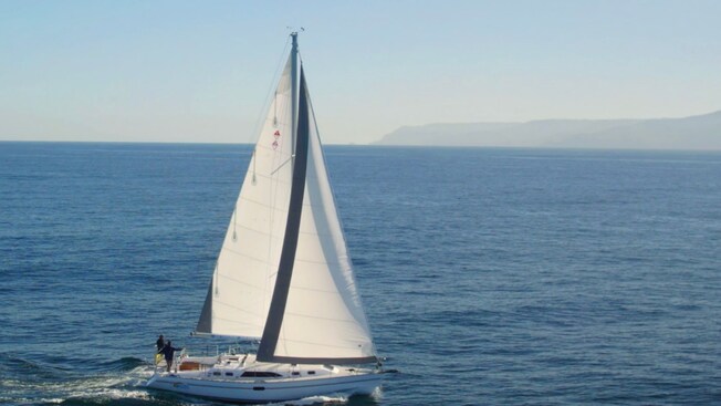 Two people standing on the deck of a sailboat as it sails along the ocean