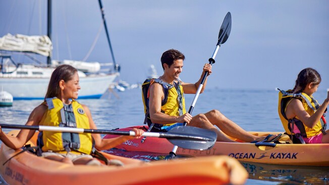 Three people kayaking near a sailboat