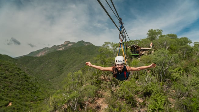 A woman smiling and holding her arms outstretched while riding a zip line head first A woman smiling and holding her arms outstretched while riding a zip line head first