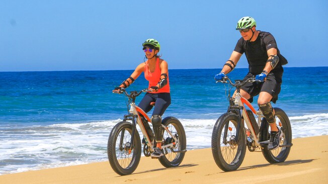 Two Guests riding electric bikes along a beach