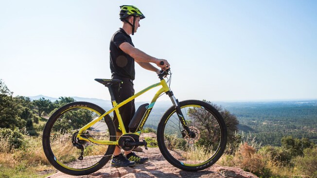 A man standing beside his electronic bike on a mountain in France