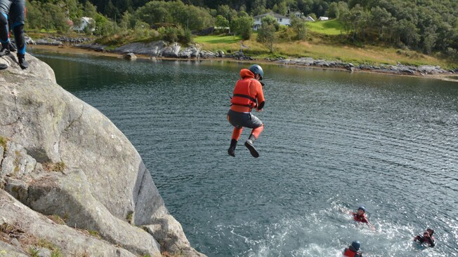 A person in a helmet and life preserver jumps into the water from a rocky ledge