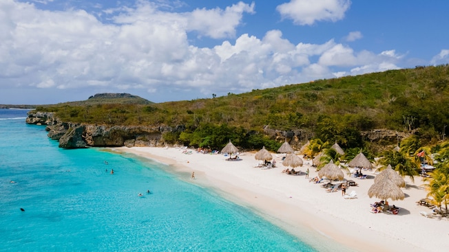 Una playa a lo largo de las orillas de Curazao con reposeras y sombrillas de paja Una playa a lo largo de las orillas de Curazao con reposeras y sombrillas de paja