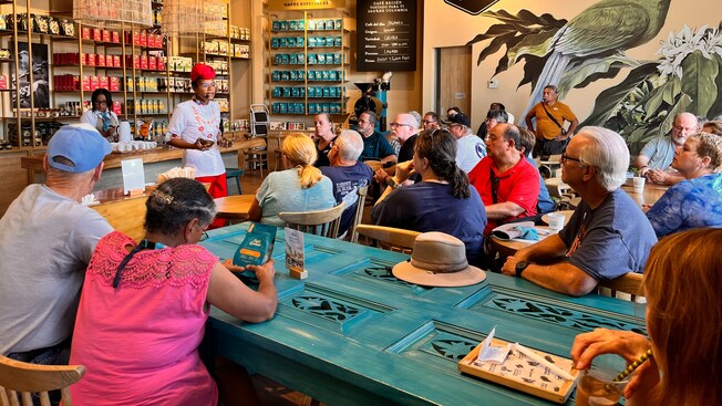A guide giving a presentation to a tour group inside a rustic coffee shop