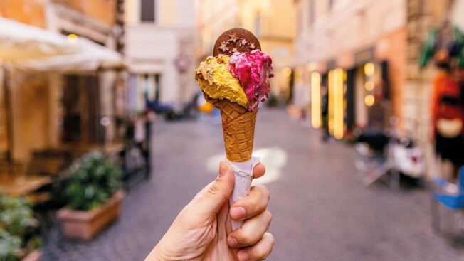 La mano de un Visitante sosteniendo un cono de gelato en medio de una calle de Civitavecchia