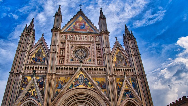 The facade of a Gothic cathedral featuring intricate mosaics, detailed carvings and tall spires