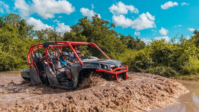 Três pessoas em um veículo 4x4 aberto passando pela lama Três pessoas em um veículo 4x4 aberto passando pela lama