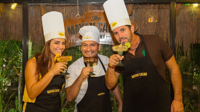 A couple wearing chef hats and drinking cocktails with the mixology expert at The Mayan Cacao Company in Cozumel, Mexico A couple wearing chef hats and drinking cocktails with the mixology expert at The Mayan Cacao Company in Cozumel, Mexico