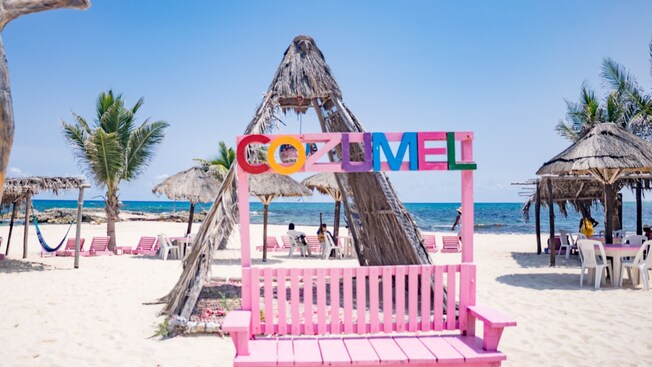 A bench with a sign that reads ‘Cozumel’ along a beach