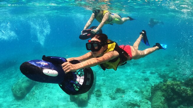 Three people snorkeling underwater behind power sea scooters