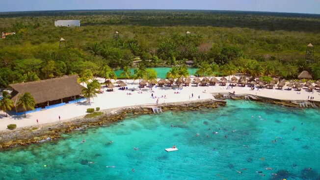Una playa tropical de arena blanca con palapas y exuberante vegetación