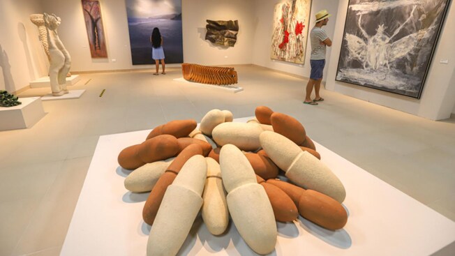 A man and a woman examine art pieces in a museum gallery filled with paintings and sculptures
