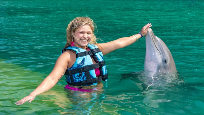 Una mujer con un chaleco salvavidas posa junto a un delfín mientras le toca la nariz en Dolphin Cove en Jamaica