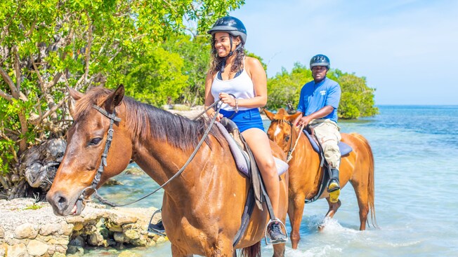 Two people riding horses at the beach