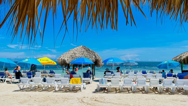Sunbathers sit in lounge chairs underneath umbrellas on a picturesque beach