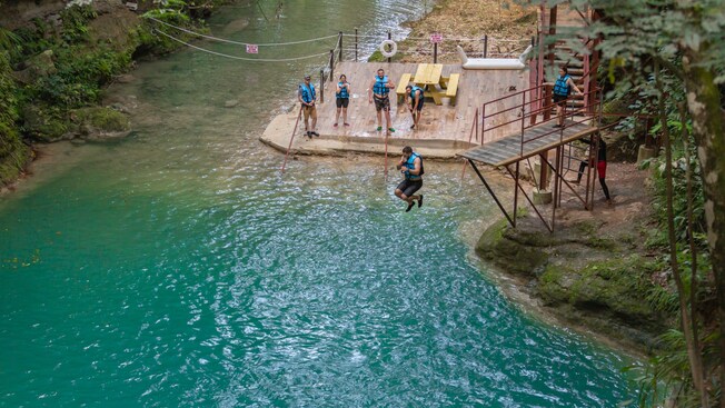 A man jumping into a swimming hole from a platform as others look on