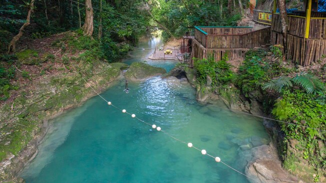 A swimming hole with a zip line and buoy rope, next to a bamboo shelter overlooking the area