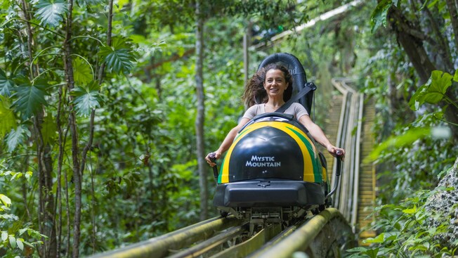 A woman strapped onto a bobsled ride amid a natural landscape and the words ‘Mystic Mountain’