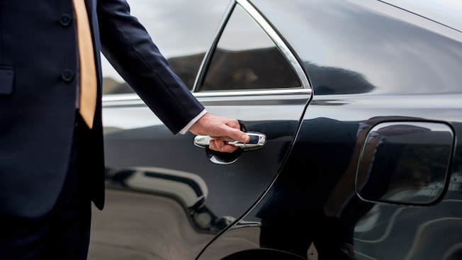 A private driver opening the door of a luxury sedan A private driver opening the door of a luxury sedan