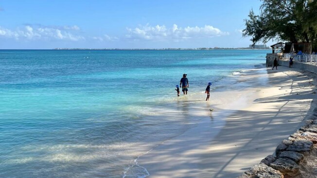 Uma família de três pessoas na água ao longo da costa de Seven Mile Beach, em Grand Cayman