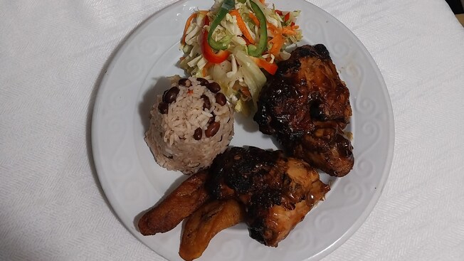 A plate of food with chicken, plantains, rice, a salad, and a tropical drink on the side