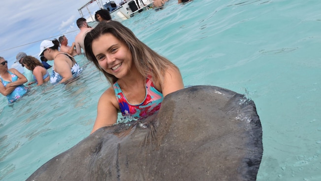 A woman standing in water with her arms cradled under a stingray A woman standing in water with her arms cradled under a stingray