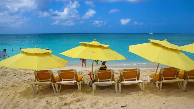 Uma pessoa sentada em uma espreguiçadeira sob um guarda-sol na Seven Mile Beach, Grand Cayman