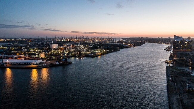 O rio Elba em Hamburgo, na Alemanha, ao anoitecer, cercado por estaleiros e pela Elbphilharmonie, a sala de concertos da cidade