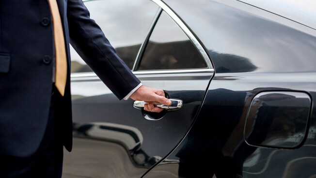 A private driver opening the door of a luxury sedan