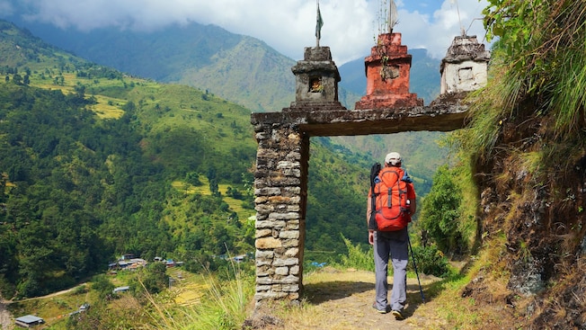 A person with a backpack walking under a stone arch, with the Norwegian mountains A person with a backpack walking under a stone arch, with the Norwegian mountains
