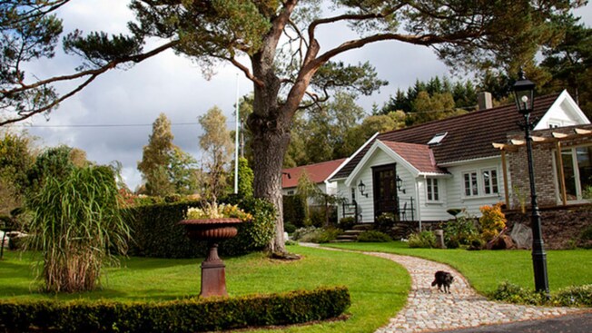 Una casa con un jardín paisajístico, que tiene un gran árbol y un camino de piedras