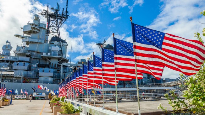 A series of American flags flying next to a Navy ship