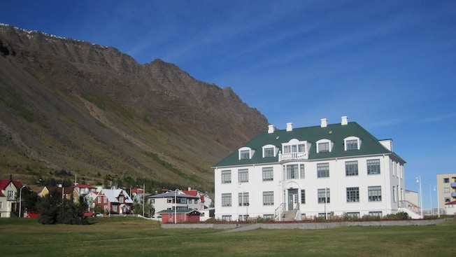 Un edificio de 4 pisos con gablete en un pueblo al pie de una ladera rocosa Un edificio de 4 pisos con gablete en un pueblo al pie de una ladera rocosa