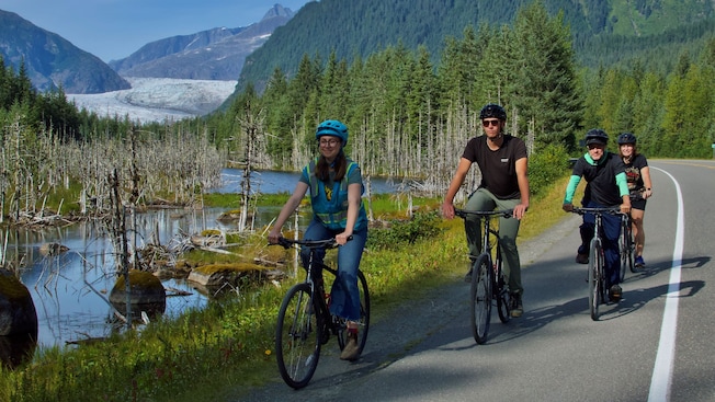 A family riding bicycles along a river with Mendenhall Glacier in the distance A family riding bicycles along a river with Mendenhall Glacier in the distance