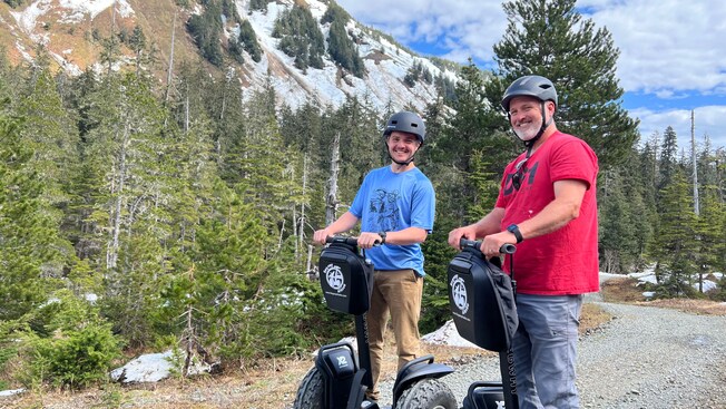 Two men ride Segways past a snow covered mountain