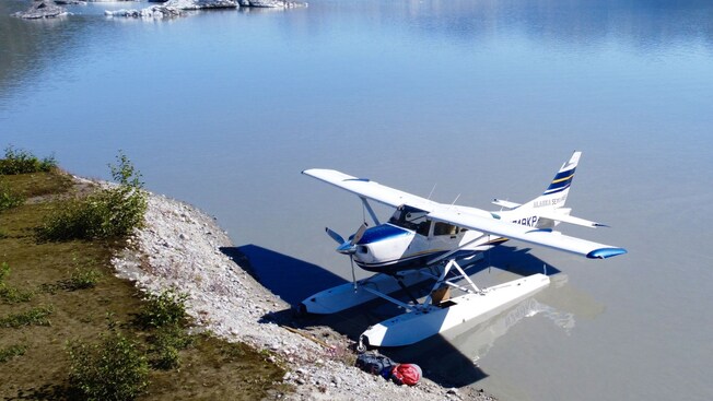 A floatplane docked on the shore, across the water from a glacier