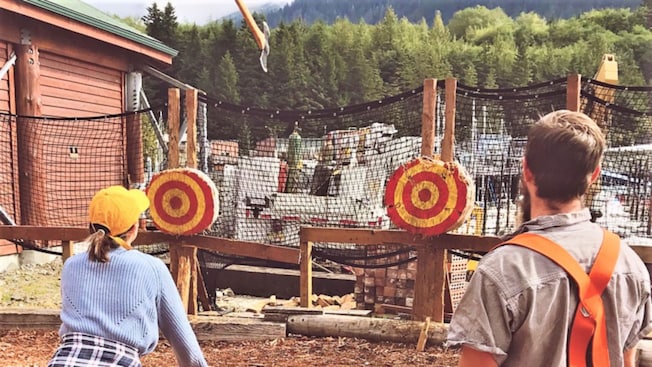 A man and a woman dressed as lumberjacks standing next to 2 target boards A man and a woman dressed as lumberjacks standing next to 2 target boards