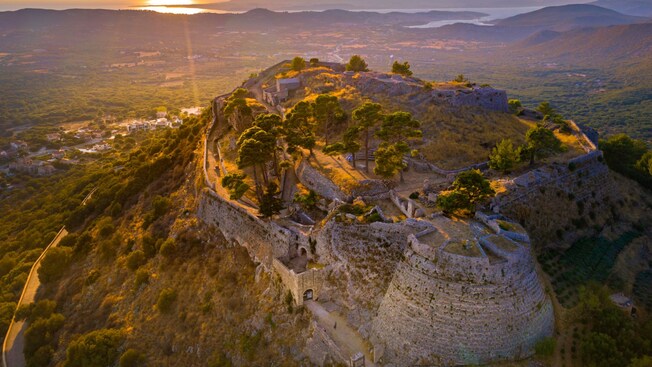 The sun setting over a lush valley and mountain cliff with castle ruins