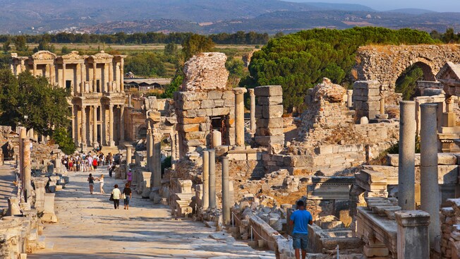 Gente caminando por un camino de piedra bordeado con las ruinas de una ciudad antigua