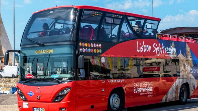 Un autobús de dos pisos con techo abierto frente al monumento del Cristo Rei en Lisboa