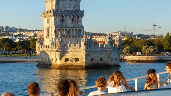 A group of people looking at Belém Tower, a structure surrounded by water
