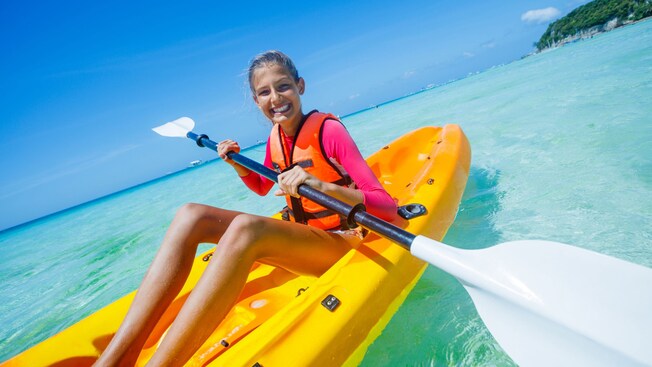 A young girl smiles while paddling a kayak in shallow waters