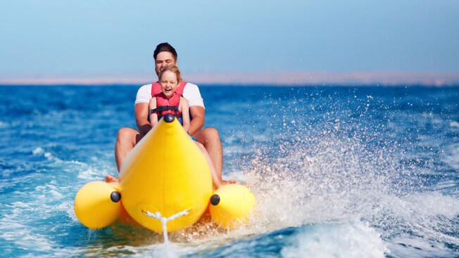 A man and a small child riding an inflatable watercraft shaped like a banana