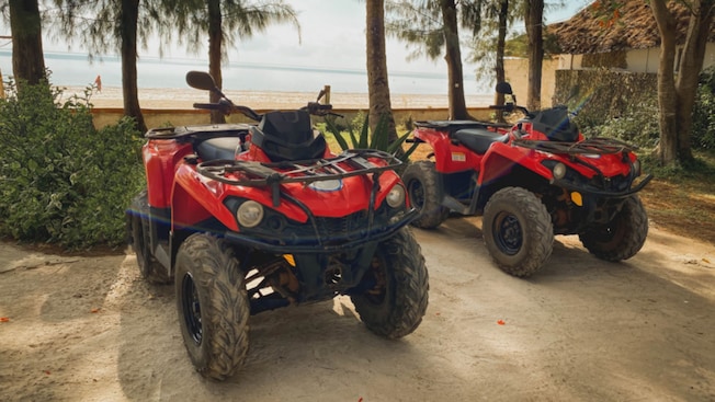 Two ATVs parked next to a building near a beach Two ATVs parked next to a building near a beach