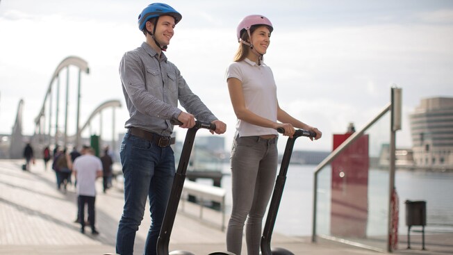 2 people in helmets each riding a motorized 2 wheel transporter