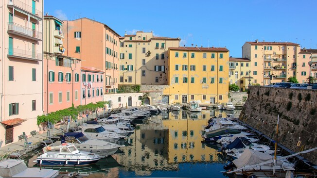 A water canal lined with docked boats runs past vibrant multi story buildings