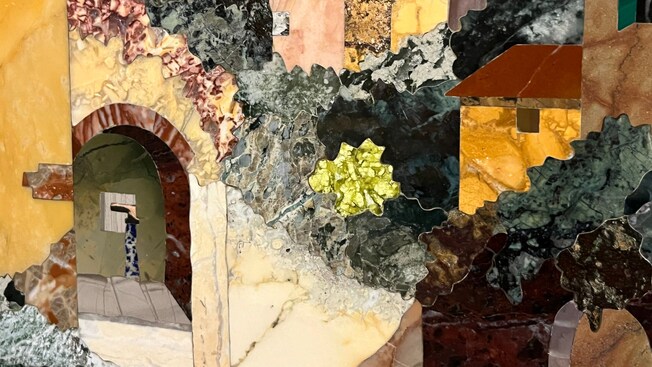 A detail of a mosaic displaying an arch, houses and vegetation