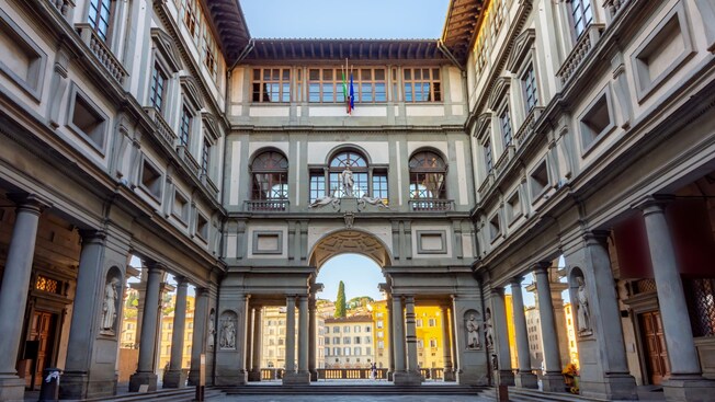 A courtyard featuring columns and arches with the Uffizi Gallery in Florence, Italy in the background